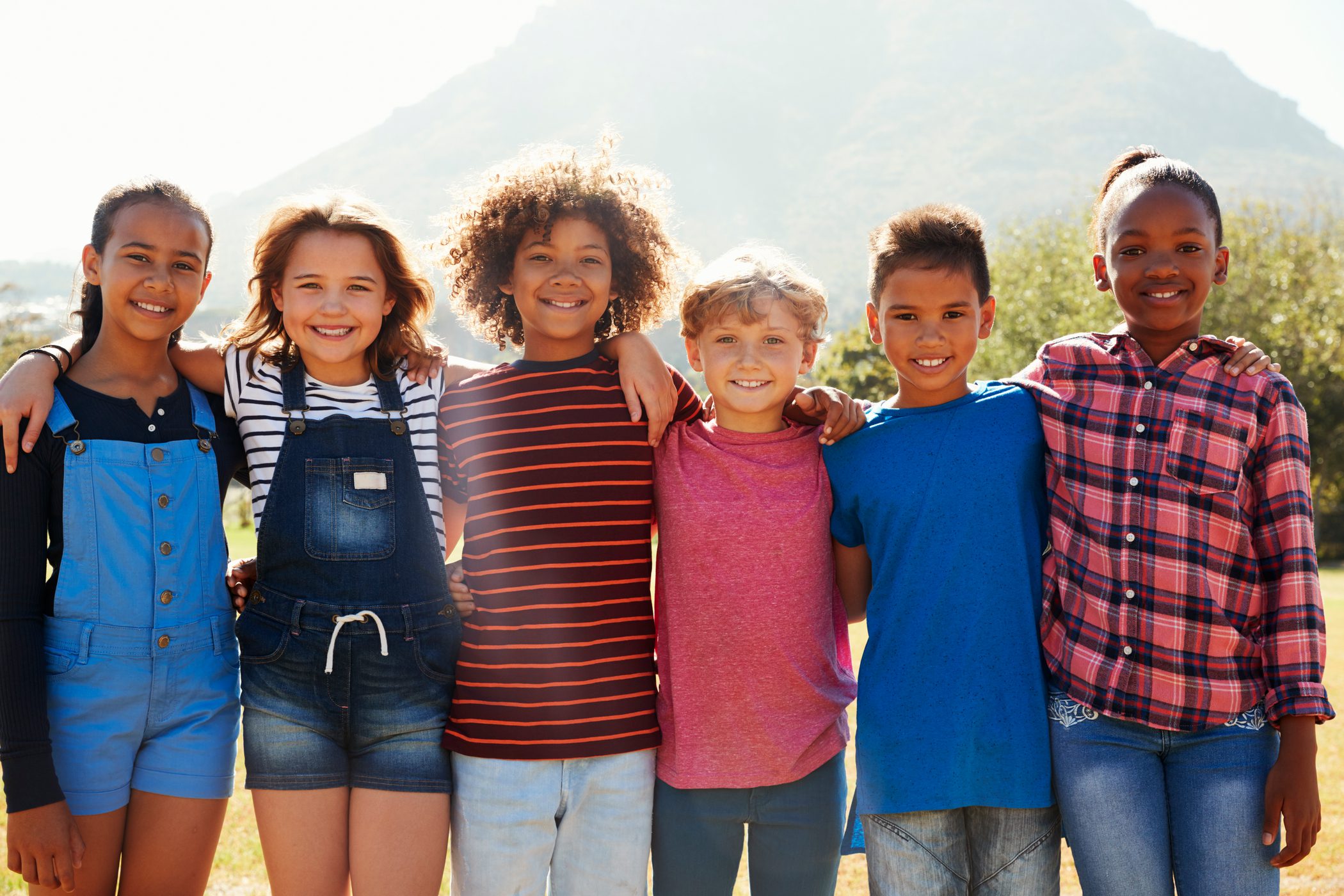 Group of children stand side-by-side smiling while playing outside on a sunny day